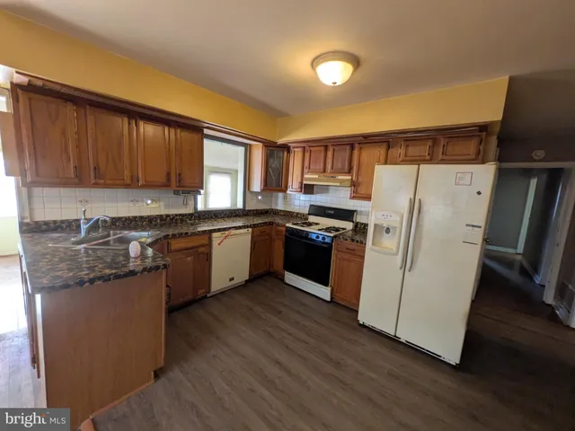 a kitchen with granite countertop wooden floors a stove a sink and a white refrigerator