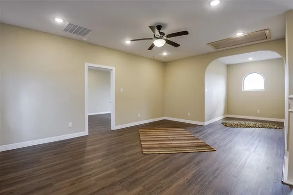 a view of an empty room with wooden floor and a ceiling fan