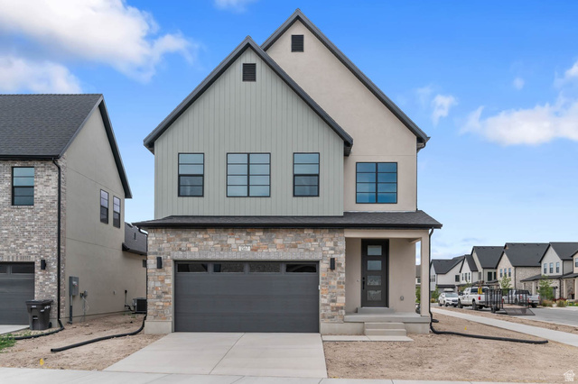 1567 North 3250 West Provo, UT 84601 - Photo 1 of 22 Contemporary residence featuring a two-car garage with a dark gray door, stone facade accents, a covered entry porch, and black-framed windows