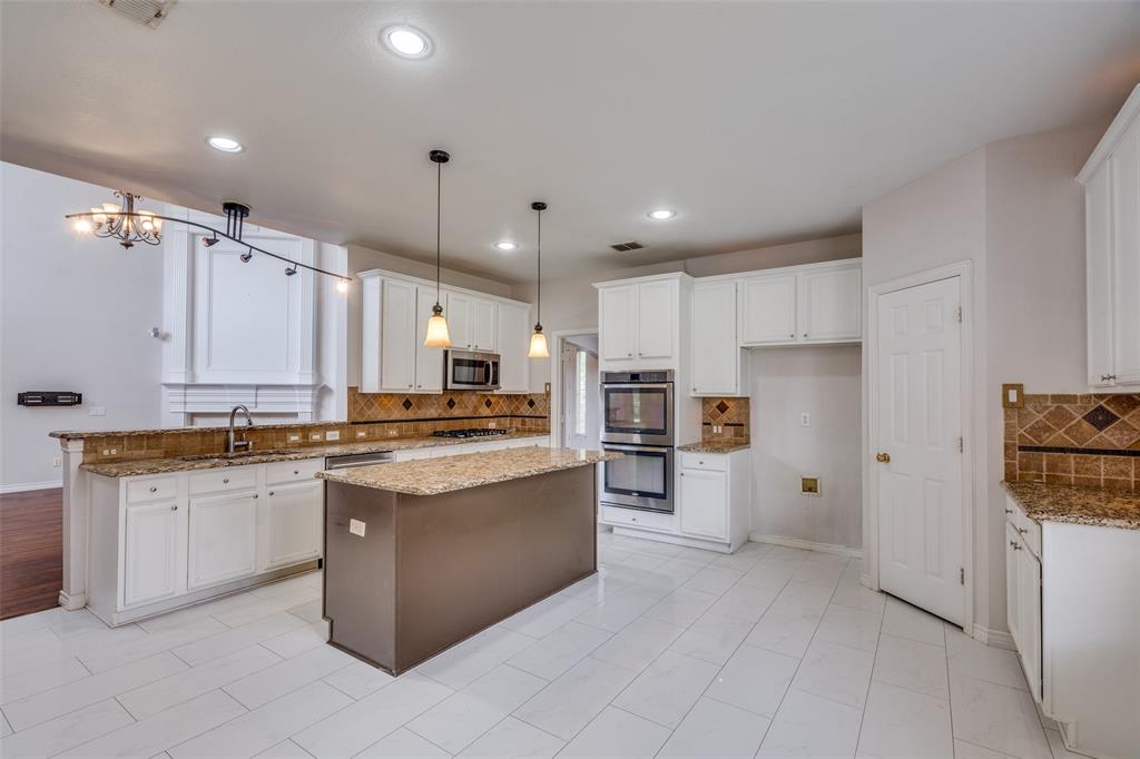 3421 Neiman Road Plano, TX 75025 - Photo 13 of 40 Kitchen with stainless steel appliances, a kitchen island, backsplash, white cabinetry, and light stone counters