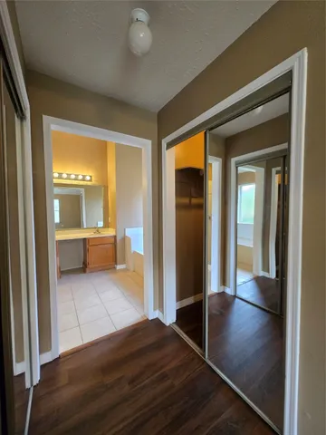 a view of a hallway to an empty room with wooden floor and a kitchen