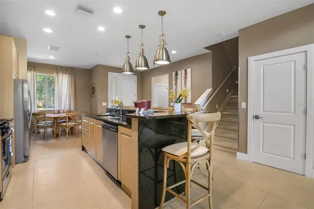 a kitchen with stainless steel appliances kitchen island granite countertop dining table chairs and a refrigerator