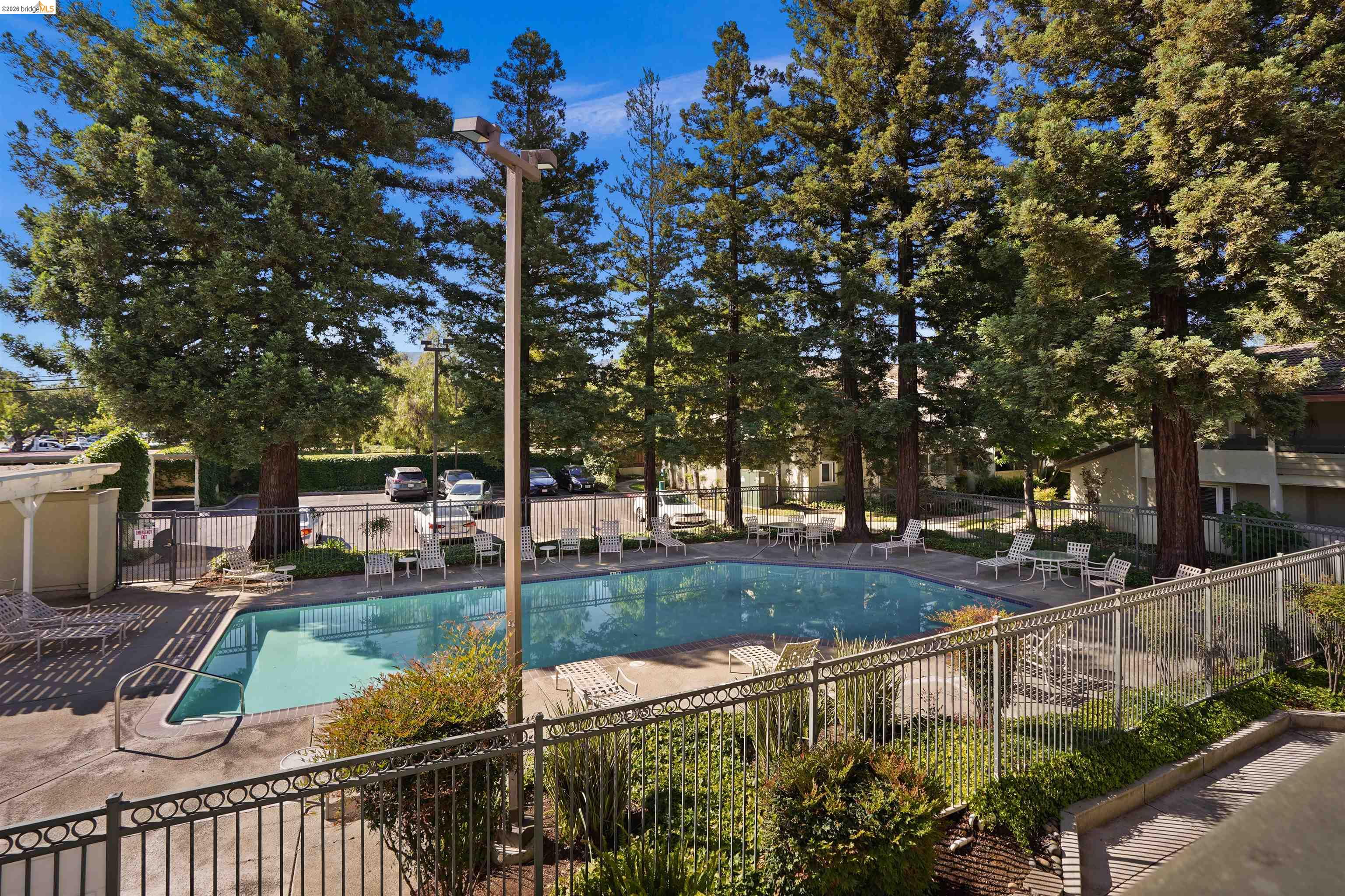 1505 Kirker Pass Road, Unit 214 Concord, CA 94521 - Photo 1 of 55 Community swimming pool surrounded by mature trees, featuring a paved deck, perimeter fencing, and seating areas