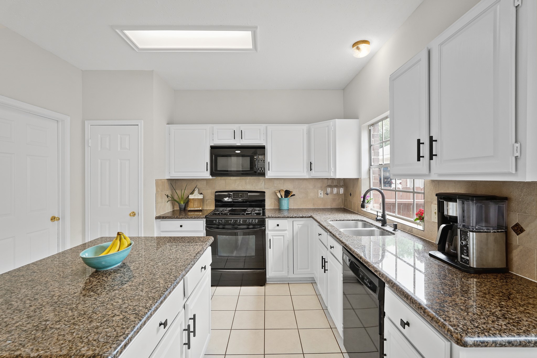 16114 Kintyre Point Road Houston, TX 77095 - Photo 37 of 44 This kitchen features bright white cabinetry paired with sleek black appliances and granite countertops. It includes a spacious island with additional storage, a large window for natural light, and modern fixtures, creating a welcoming and functional space.