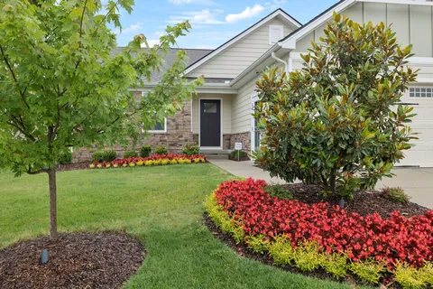 a front view of a house with lots of flowers and trees