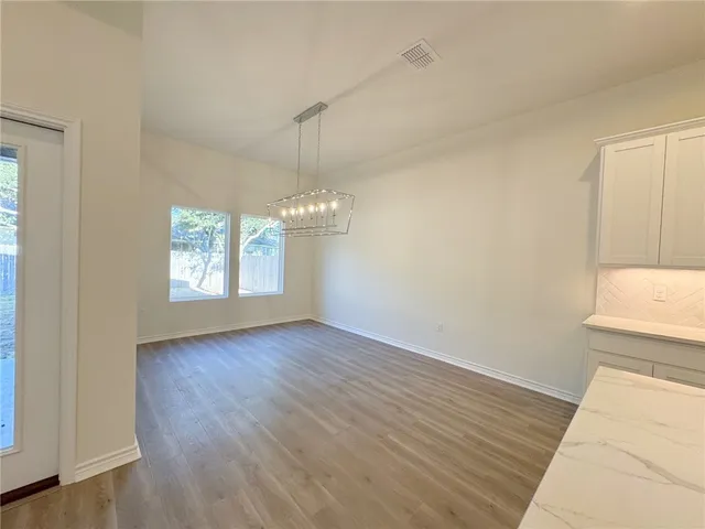 an empty room with wooden floor chandelier and windows