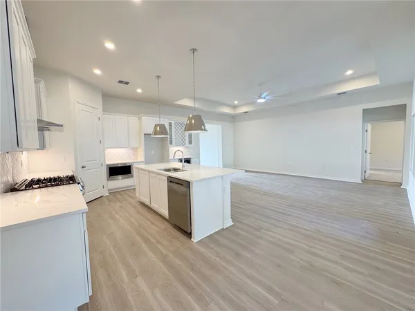 a large white kitchen with a stove a sink dishwasher and a refrigerator with wooden floor