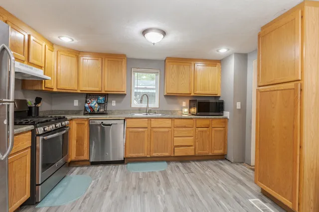 a kitchen with stainless steel appliances granite countertop a refrigerator a stove top oven a sink and dishwasher with wooden floor