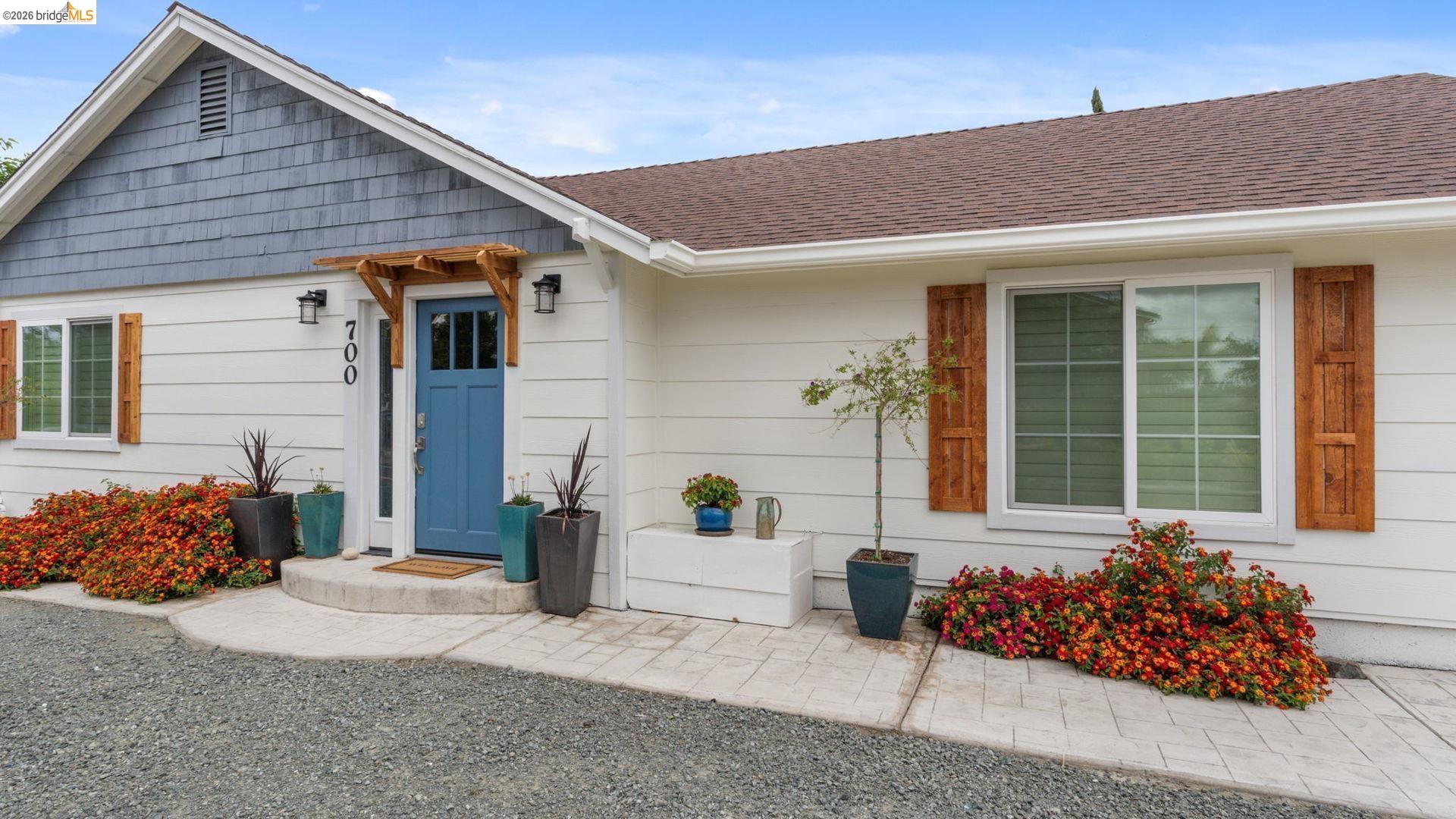 700 Brownstone Road Oakley, CA 94561 - Photo 53 of 58 Exterior facade featuring white siding with contrasting blue shingle accents, a blue paneled entry door with an overhead wooden trellis, and white-framed windows with decorative wooden shutters