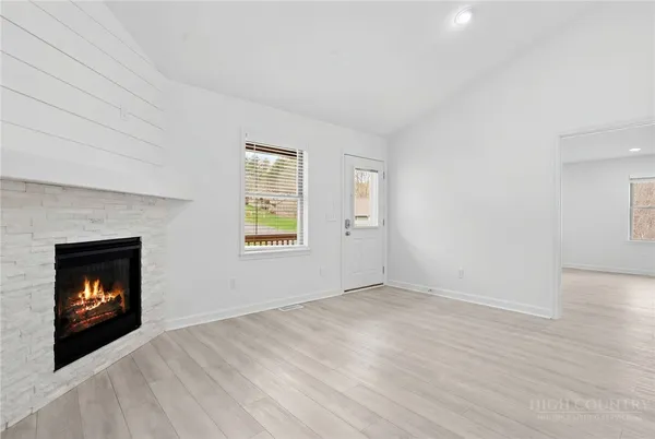 a view of an empty room with wooden floor fireplace and a window