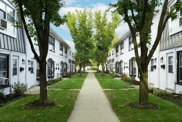 a view of a white house next to a yard with big trees