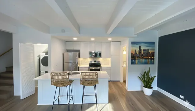 a kitchen with stainless steel appliances kitchen island granite countertop a refrigerator a stove top oven a dining table and chairs with wooden floor