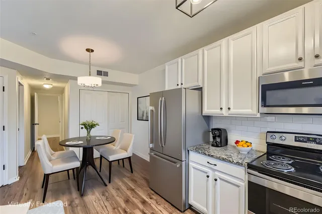 a kitchen with stainless steel appliances granite countertop a stove a refrigerator a microwave a dining table and chairs with wooden floor