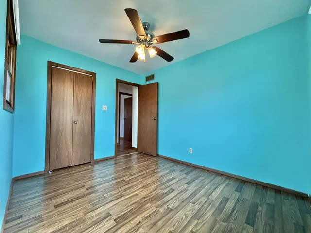 a view of an empty room with wooden floor and a ceiling fan