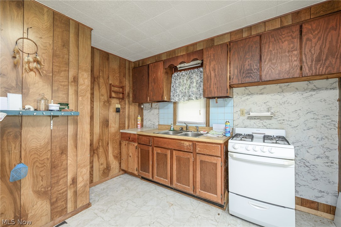 8386 Yale Road Rootstown, OH 44272 - Photo 13 of 46 Kitchen featuring wood-panel walls, wood cabinetry, a dual basin stainless steel sink, a tiled backsplash, and a white freestanding range