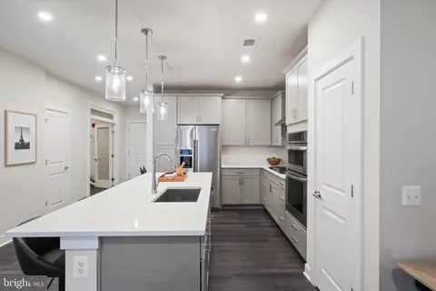 a large kitchen with stainless steel appliances kitchen island a refrigerator a sink dishwasher a stove and white cabinets with wooden floor