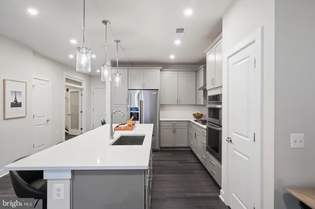 a large kitchen with stainless steel appliances kitchen island a refrigerator a sink dishwasher a dining table and chairs with wooden floor