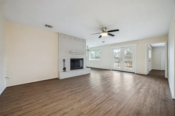 an empty room with fireplace wooden floor chandelier fan and windows