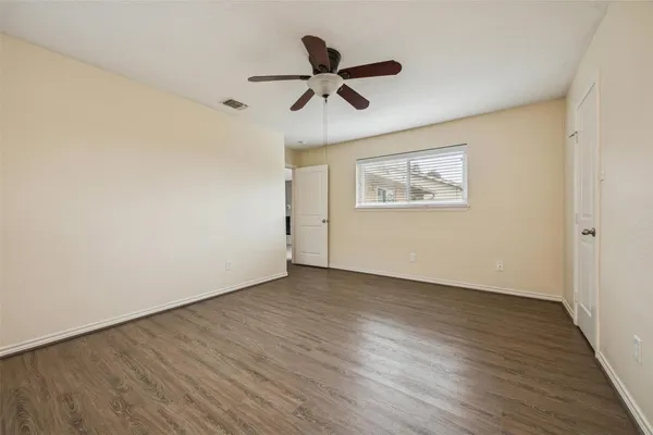 a view of an empty room with wooden floor and a ceiling fan