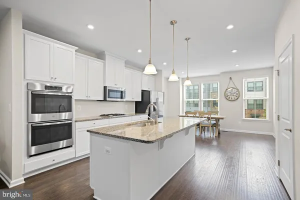 a kitchen with stainless steel appliances granite countertop a stove top oven a sink dishwasher a dining table and chairs with wooden floor