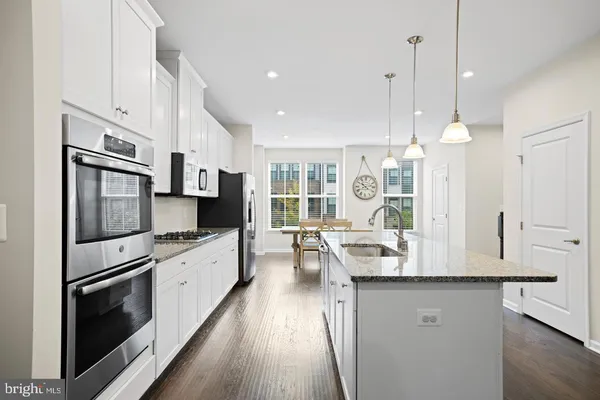a kitchen with kitchen island granite countertop a stove a sink a refrigerator and white cabinets with wooden floor