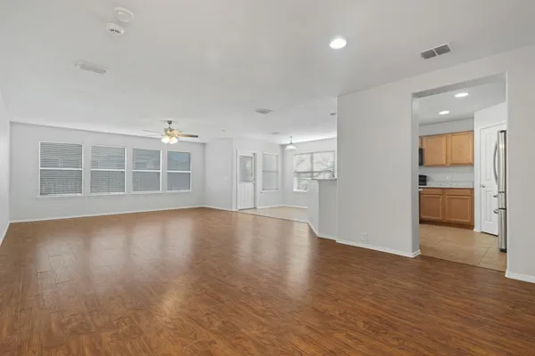 a view of empty room with wooden floor and kitchen