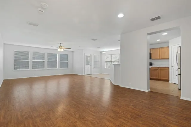 a view of empty room with wooden floor and kitchen