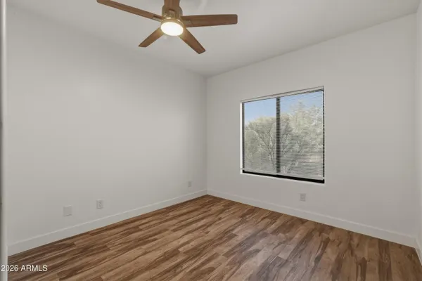 a view of an empty room with wooden floor and a ceiling fan