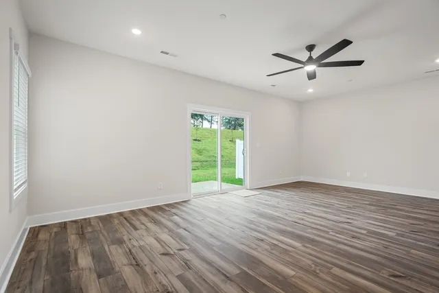 an empty room with wooden floor fan and windows