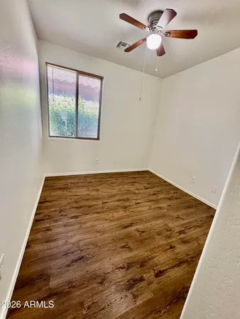 a view of an empty room with wooden floor and a ceiling fan