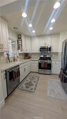 a kitchen with stainless steel appliances granite countertop a stove top oven a sink dishwasher a refrigerator and a dining table with wooden floor