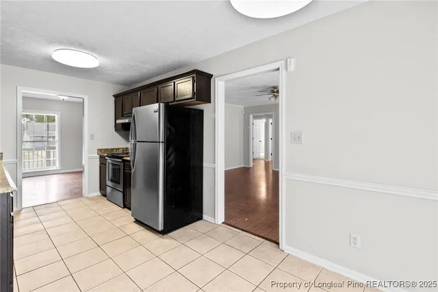a view of a refrigerator in kitchen and an empty room with wooden floor
