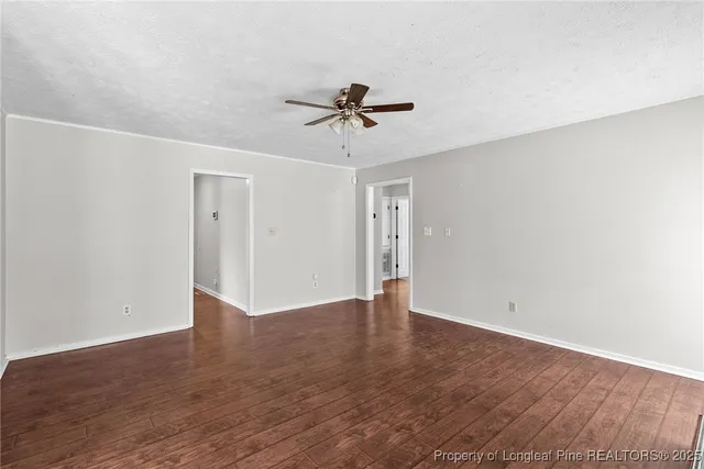 an empty room with wooden floor ceiling fan and windows