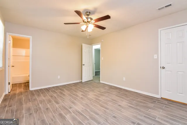 a view of an empty room with wooden floor and a ceiling fan