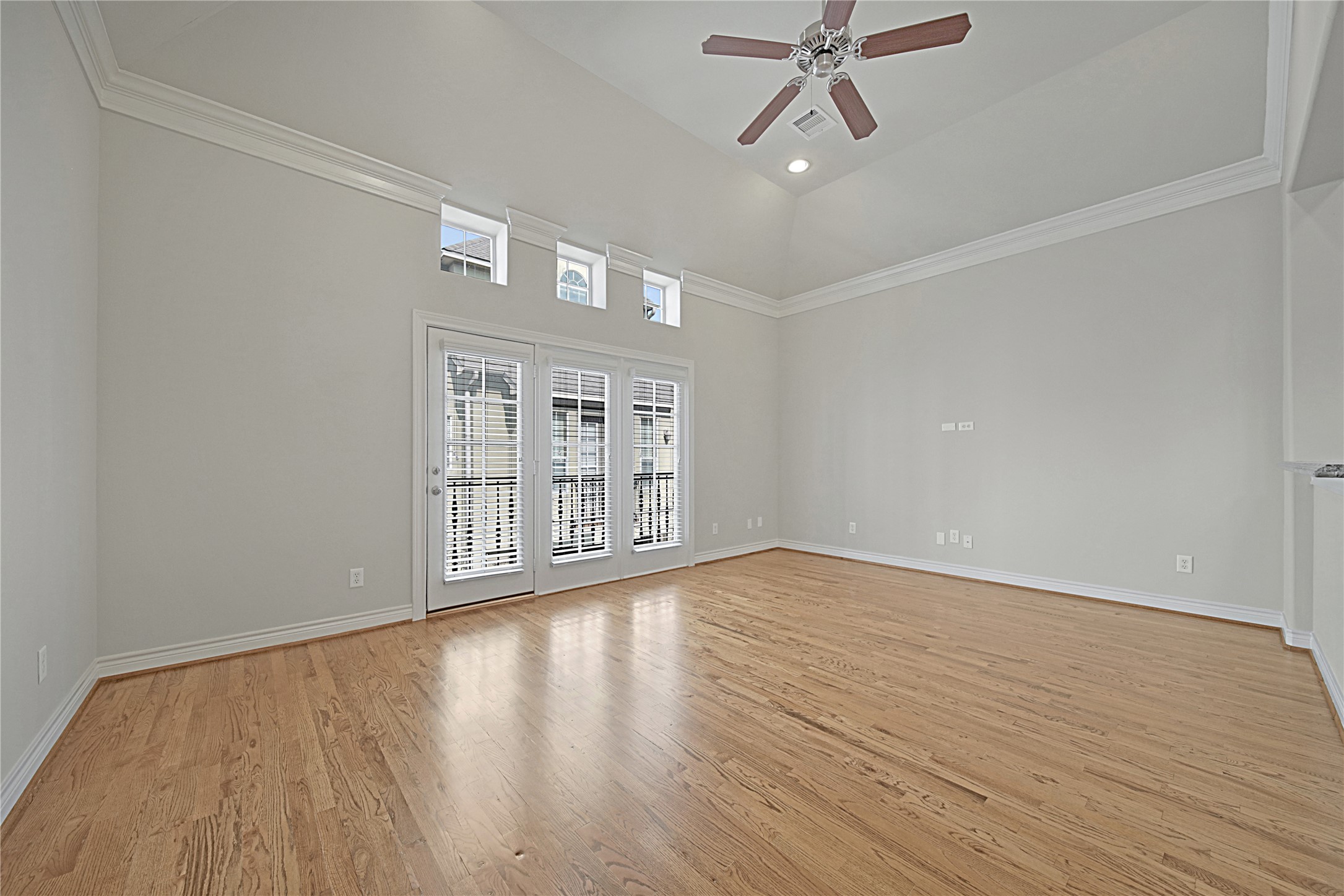 2726 Sherwin Street Houston, TX 77007 - Photo 5 of 23 This spacious room features high ceilings, hardwood floors, and abundant natural light from multiple windows and glass doors leading to a balcony. A ceiling fan adds comfort.