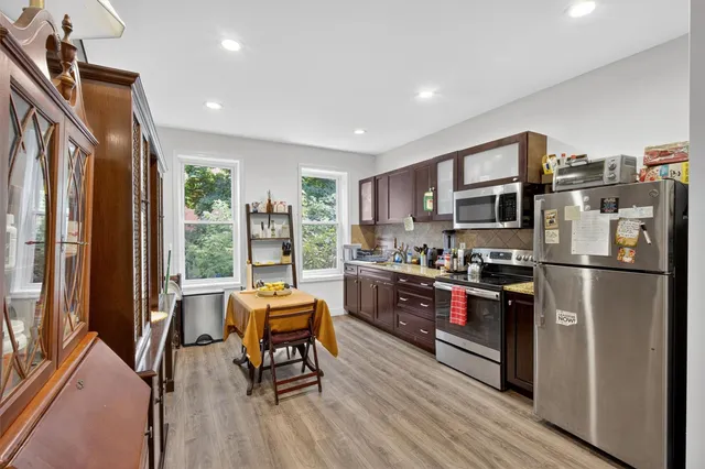 a kitchen with stainless steel appliances granite countertop a refrigerator a stove top oven a sink dishwasher a dining table and chairs with wooden floor