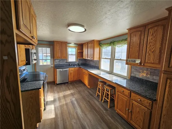 a kitchen with stainless steel appliances granite countertop wooden cabinets a sink dishwasher a stove and a refrigerator with wooden floor