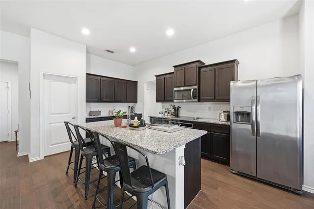 a kitchen with stainless steel appliances granite countertop a stove a sink a microwave a refrigerator and chairs