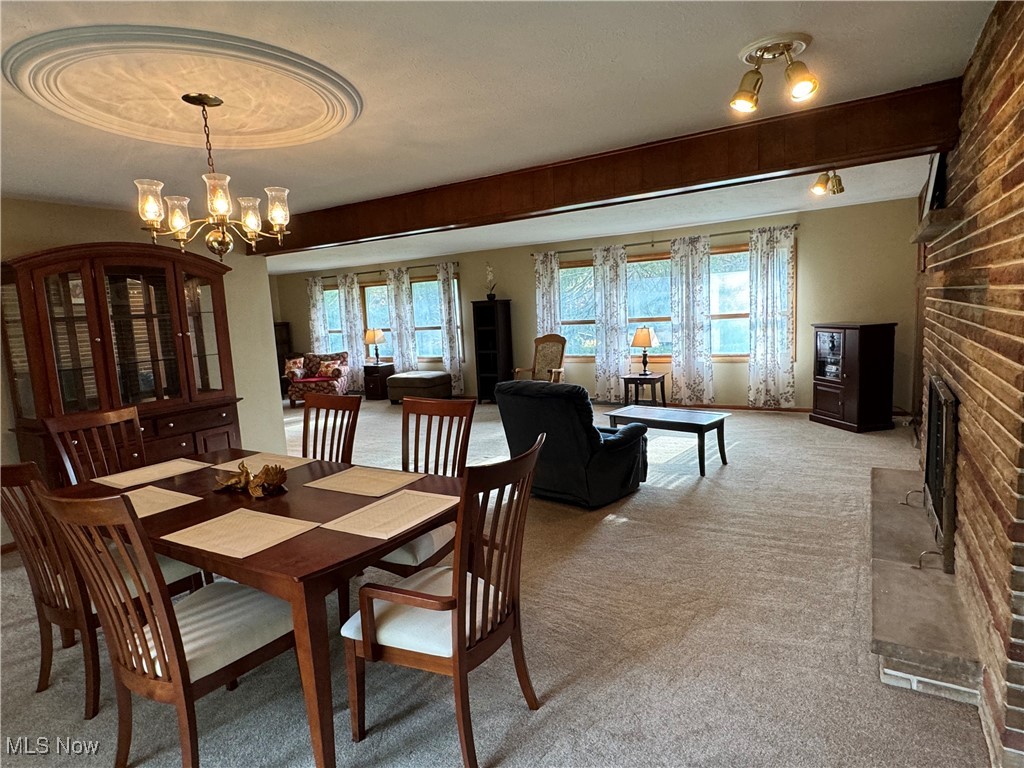 Carpeted dining area featuring a fireplace, a wealth of natural light, and a chandelier