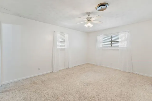 an empty room with chandelier fan and windows