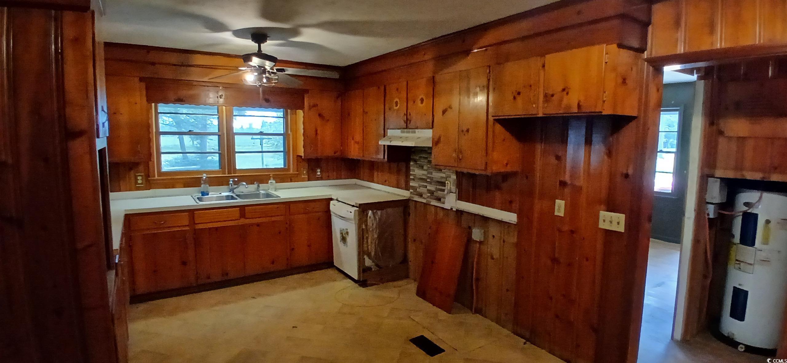 1206 French Road Mullins, SC 29574 - Photo 18 of 31 Kitchen with under cabinet range hood, brown cabinets, ceiling fan, wood walls, and electric water heater