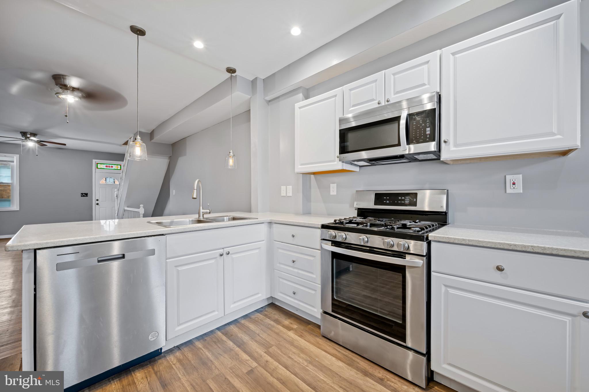 628 Savage Street Baltimore, MD 21224 - Photo 13 of 45 a kitchen with stainless steel appliances granite countertop a stove a microwave and white cabinets