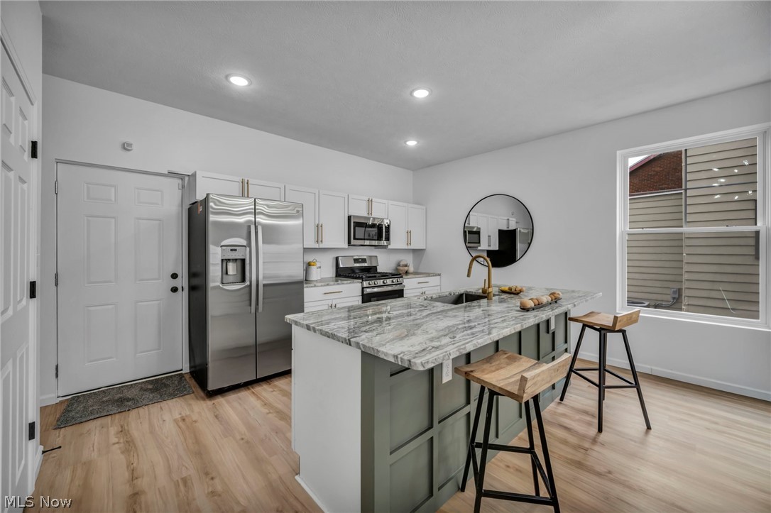 3633 Pennington Road Cleveland, OH 44120 - Photo 13 of 34 Kitchen featuring white cabinets, stainless steel appliances, light stone counters, a kitchen breakfast bar, and light wood-style floors