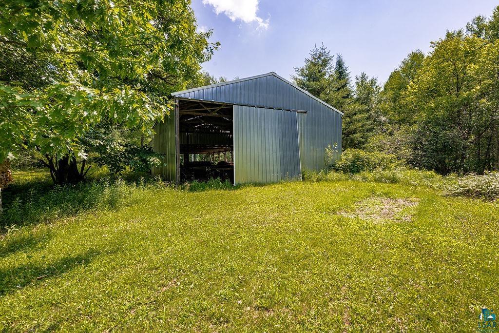 2592 Strandberg Road Barnum, MN 55707 - Photo 27 of 44 Corrugated metal barn with a pitched roof and a large sliding entry door, set on a grassy expanse surrounded by mature trees