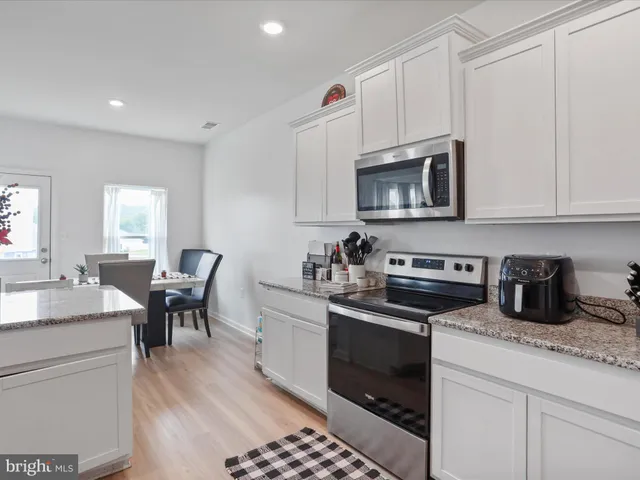 a kitchen with granite countertop a stove top oven a sink dishwasher and white cabinets with wooden floor