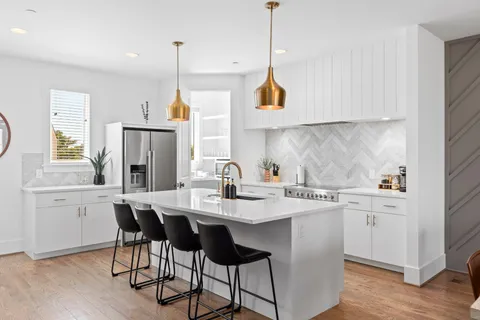 a kitchen with stainless steel appliances granite countertop a sink a stove a refrigerator and white cabinets with wooden floor