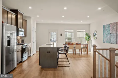 a living room with stainless steel appliances furniture wooden floor and a view of kitchen