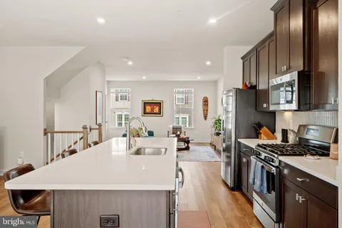 a large kitchen with stainless steel appliances a stove a sink a refrigerator and a dining table with wooden floor