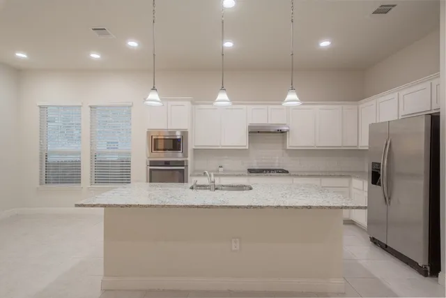 a large kitchen with kitchen island a large counter top stainless steel appliances and cabinets