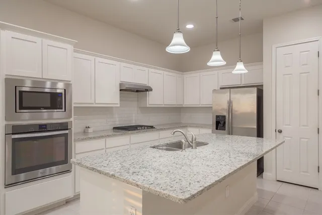 a kitchen with kitchen island granite countertop a sink a counter space appliances and cabinets